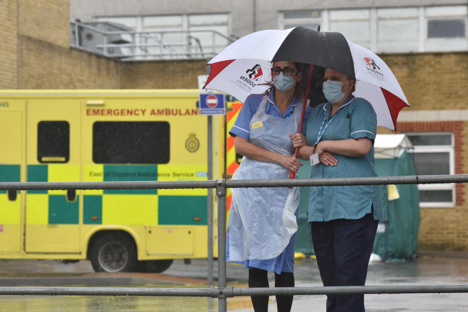 SOUTHEND ON SEA, ENGLAND  - APRIL 28: Two nurses stand under an umbrella during the pouring rain outside Southend Hospital during the minute's silence for key workers who have died during the Coronavirus on April 28, 2020 in Southend on Sea, United Kingdom. The moment of silence, commemorating the key workers who have died during the Covid-19 pandemic, was timed to coincide with International Workers' Memorial Day. At least 90 NHS workers are reported to have died in the last month, in addition to transport employees and other key workers. (Photo by John Keeble/Getty Images)