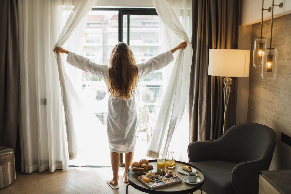 view from behind of woman opening curtains in hotel room morning awakening