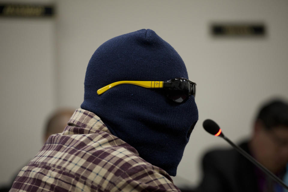 A witness, wearing a ski mask and dark sunglasses to protect his identity, testifies during the El Aguacate Massacre trial in Chimaltenango, Guatemala, Thursday, March 13, 2014. In November 1988 in the mountainous area of western Guatemala, 22 men who lived in the village of El Aguacate where massacred by leftists guerillas during the Guatemalan civil war. The trial that began Thursday, is the first against an ex-guerrilla, who is charged with taking part in the massacre. (AP Photo/Moises Castillo)