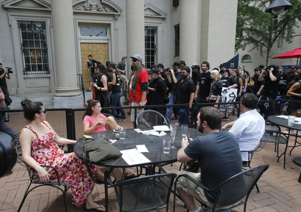 A group, Anti-fascism demonstrators, march past lunchtime diners in the downtown area in anticipation of the anniversary of last year's Unite the Right rally in Charlottesville, Va., Saturday, Aug. 11, 2018. (AP Photo/Steve Helber)