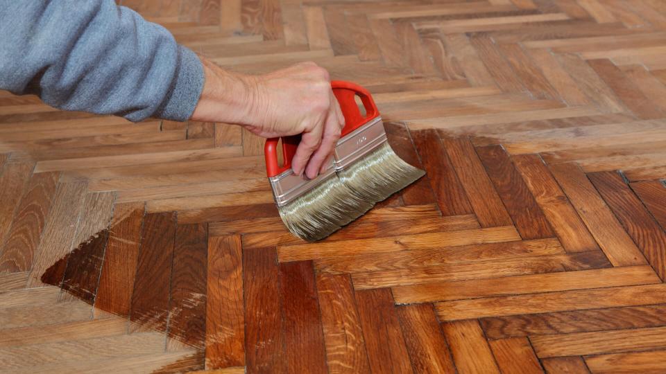 Varnishing of oak parquet floor, workers hand and brush.