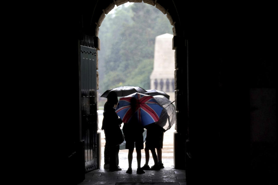 A group of people take shelter in Horse Guards Parade in central London, Sunday July 25, 2021. Thunderstorms bringing lightning and torrential rain to the south are set to continue until Monday it is forecast. (Victoria Jones/PA via AP)