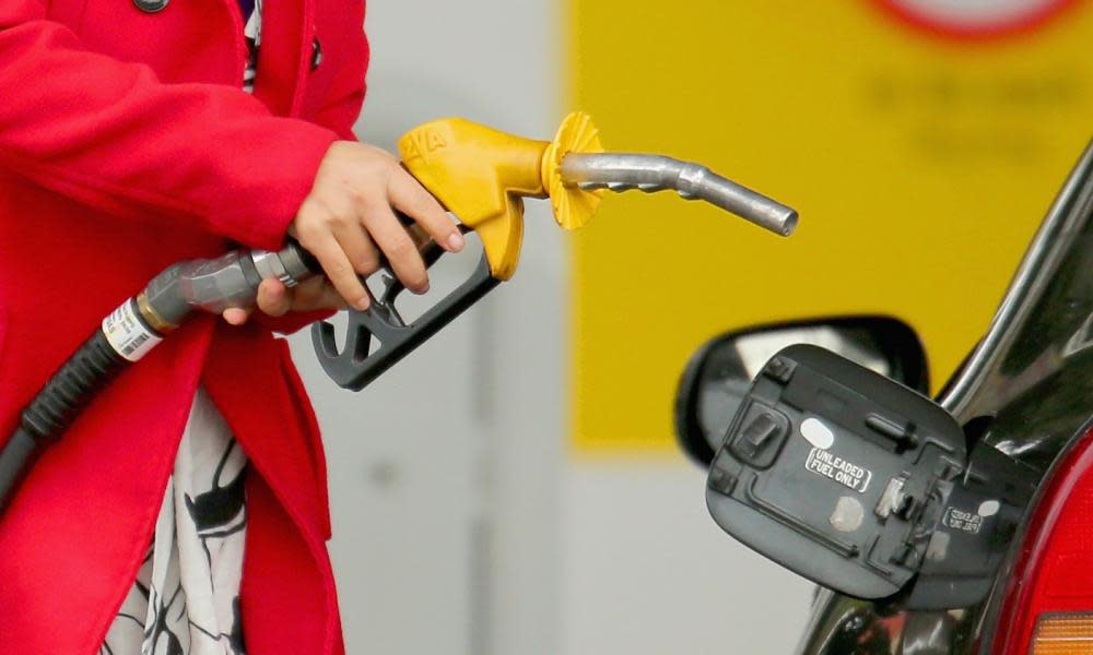 A woman uses a fuel dispenser to fill her car up with petrol at a petrol station