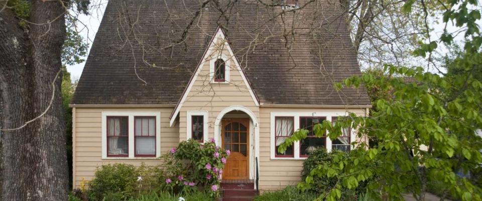 Older clapboard bungalow surrounded by green shrubs