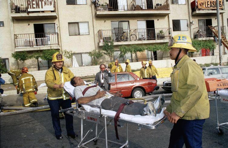 FILE - In this May 3, 1993, file photo, a survivor of an apartment complex fire is wheeled to an ambulance by Los Angeles Fire Department personnel near downtown Los Angeles. Los Angeles Police Chief Charlie Beck will announce details of arrests made in connection with the 1993 fire that killed 10 people, including seven children. Officials said that several arrests were made recently and the people remain jailed. (AP Photo/Doug Pizac,File)