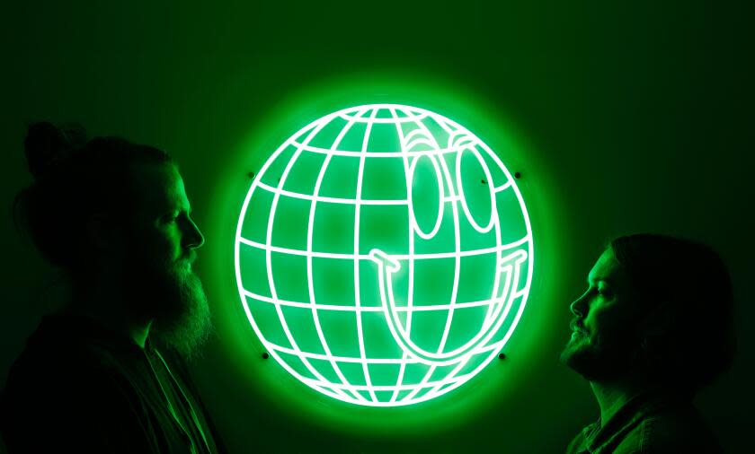 Two men stand facing each other on either side of a glowing green neon sign