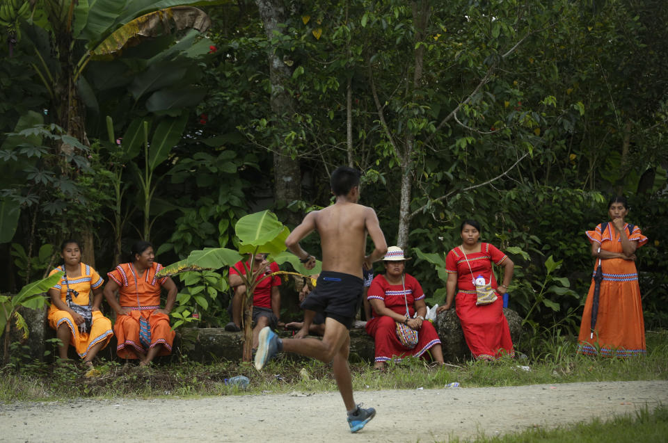 In this Nov. 26, 2018 photo, a man runs in the 10 K competition as Ngabe-Bugle women look on during the second edition of the Panamanian indigenous games in Piriati, Panama. The winner of the race will participate in the World Indigenous Games where over 30 countries and more than 2000 athletes participate. (AP Photo/Arnulfo Franco)