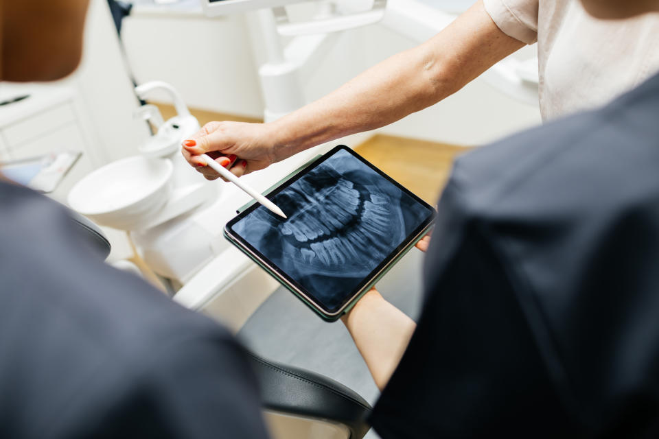 Two people examine a dental X-ray displayed on a tablet with a stylus pointing at it