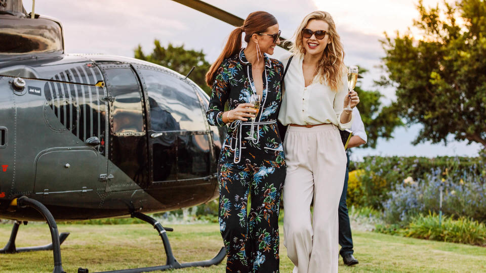 Two young women walking away from a helicopter with a glass of wine in their hands.