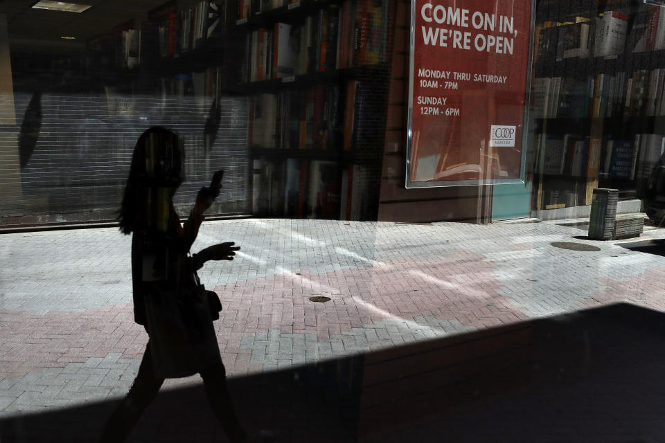 A passer-by holding a mobile device walks past a store window, Tuesday, June 16, 2020, in Cambridge, Mass. According to the Commerce Department U.S. retail sales jumped by a record 17.7% from April to May, with spending partially rebounding after the coronavirus had shut down businesses, flattened the economy and paralyzed consumers during the previous two months. (AP Photo/Steven Senne)