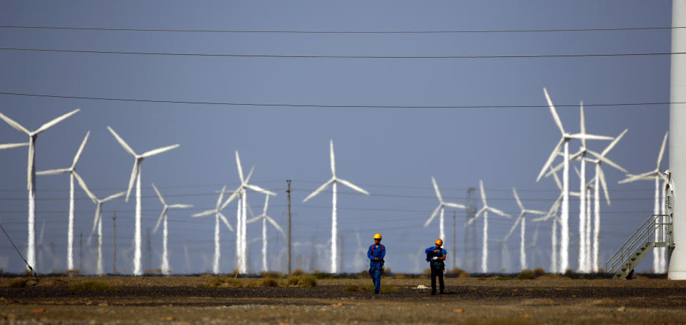 Workers walk near wind turbines for generating electricity, at a wind farm in Guazhou, China. (Photo: Carlos Barria / Reuters)