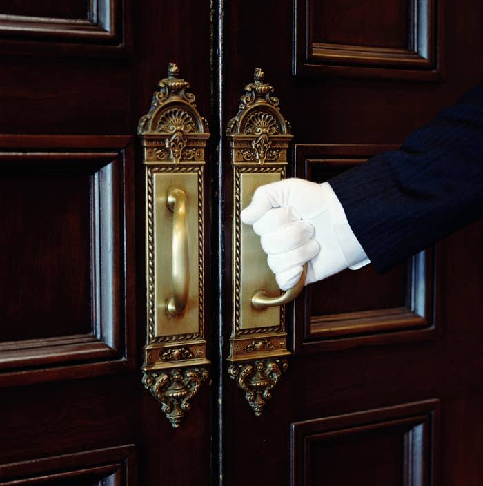 A butler's gloved hand opening a door