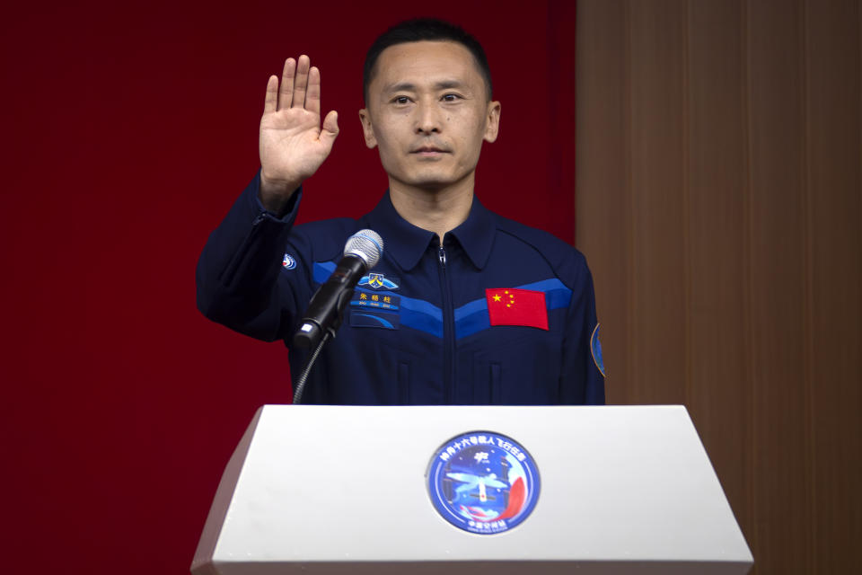 Zhu Yangzhu, a Chinese astronaut for the upcoming Shenzhou-16 mission waves as he stands behind glass during a meeting with the press at the Jiuquan Satellite Launch Center in northwest China on Monday, May 29, 2023. China's space program plans to land astronauts on the moon before 2030, a top official with the country's space program said Monday. (AP Photo/Mark Schiefelbein)