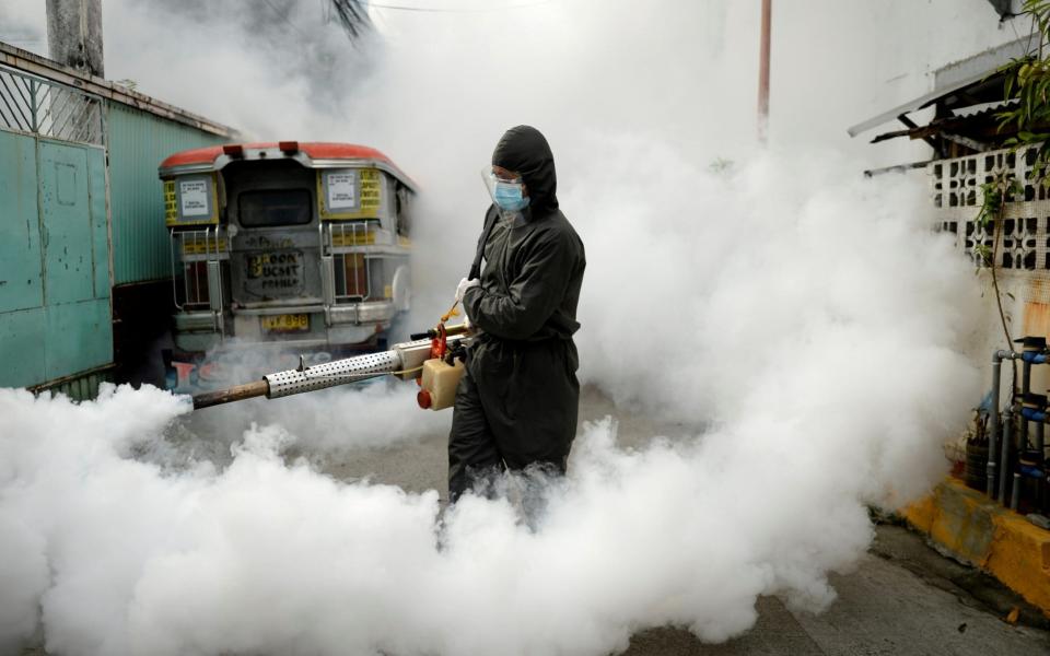 A worker disinfects a street as a preventive measure against the spread of coronavirus at a village in Manila - Reuters