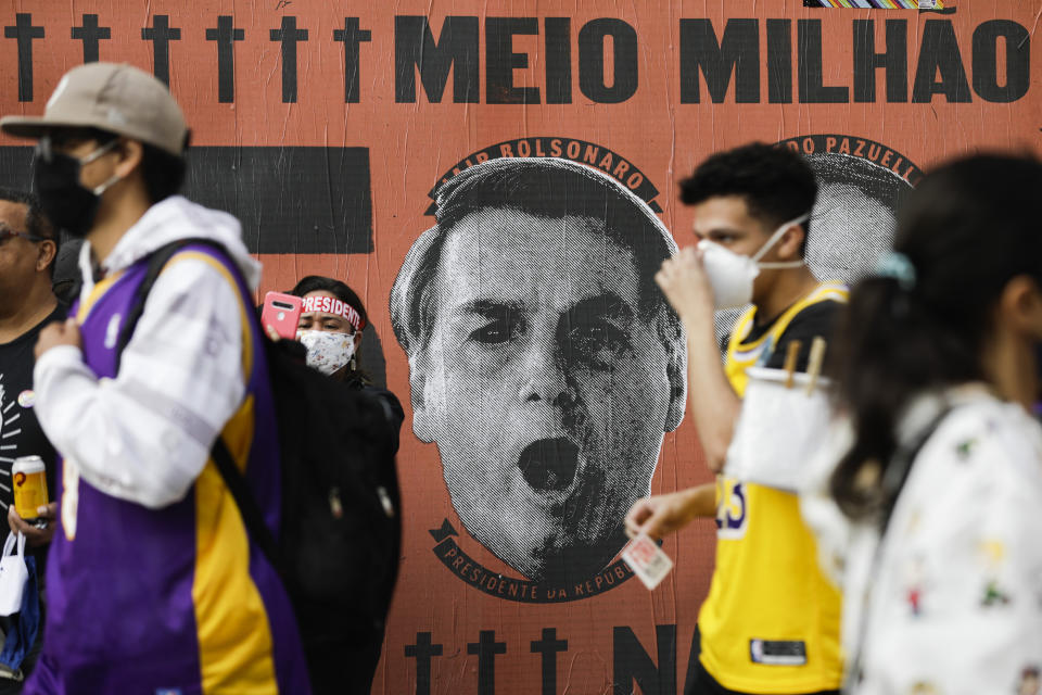 FILE - In this June 19, 2021 file photo, demonstrators walk past a mural depicting the face of Brazilian President Jair Bolsonaro during a demonstration against Bolsonaro's handling of the coronavirus pandemic and economic policies protesters say harm the interests of the poor and working-class on Paulista Avenue in Sao Paulo, Brazil. In the first quarter of 2021, Brazil saw its highest unemployment and economic inequality in at least nine years, with the cost of living surging and tent cities and shantytowns emerging. (AP Photo/Marcelo Chello, File)