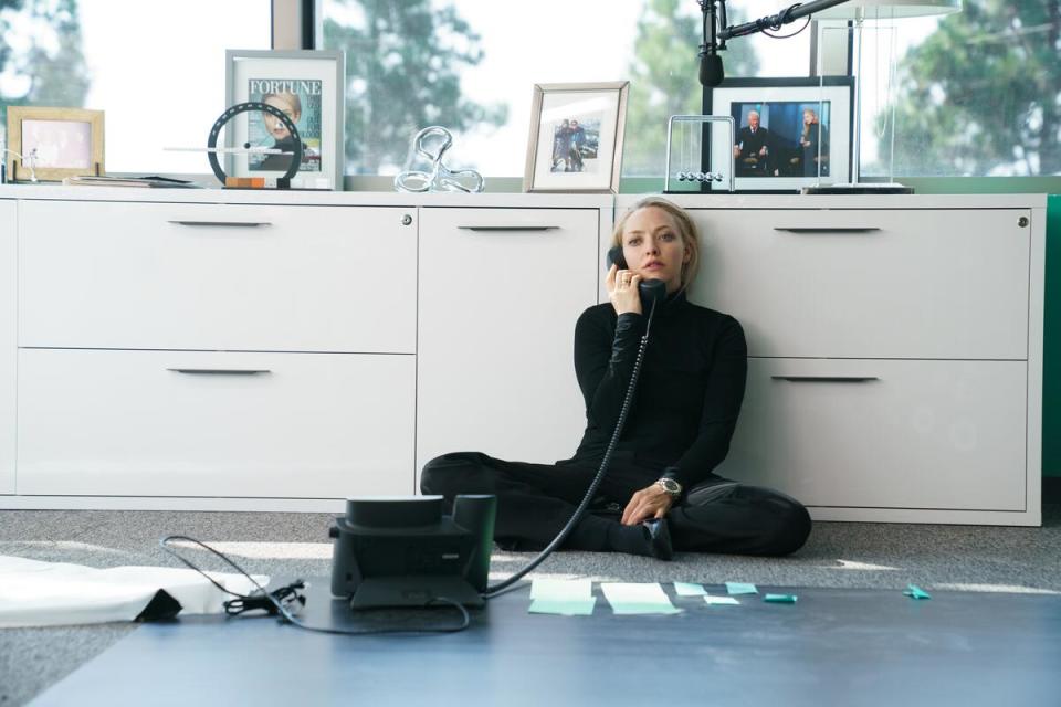 Amanda Seyfried dressed in black on the phone sitting on the floor