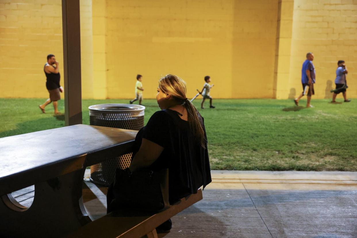 A woman sitting at a picnic table as people walk by on the grass in the background