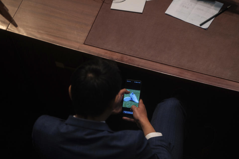 A lawmaker watches his phone during the second reading of the Basic Law Article 23 legislation at the Legislative Council in Hong Kong, Tuesday, March 19, 2024. (AP Photo/Louise Delmotte)