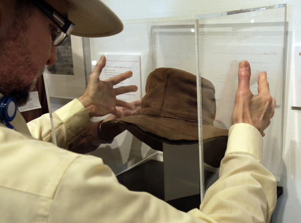 Museum Installer Rene Ronda places a protective plexiglass cube cover over a hat by designer by Edith Head, from the 1975 movie "Rooster Cogburn," as part of the "Katharine Hepburn: Dressed for Stage and Screen" exhibit in the New York Public Library for the Performing Arts at Lincoln Center, Tuesday, Oct. 16, 2012. (AP Photo/Richard Drew)