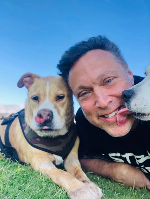 A man smiles with a pit bull while getting kissed by another dog. (Michael Levitt / Michael Levitt Productions)