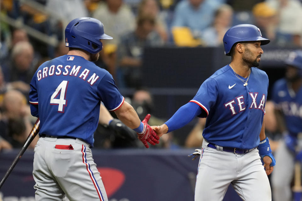 Texas Rangers' Marcus Semien, right, gets a hand from Robbie Grossman (4) after scoring a run on a Tampa Bay Rays error in the sixth inning of Game 1 in an AL wild-card baseball playoff series game Tuesday, Oct. 3, 2023, in St. Petersburg, Fla. (AP Photo/John Raoux)