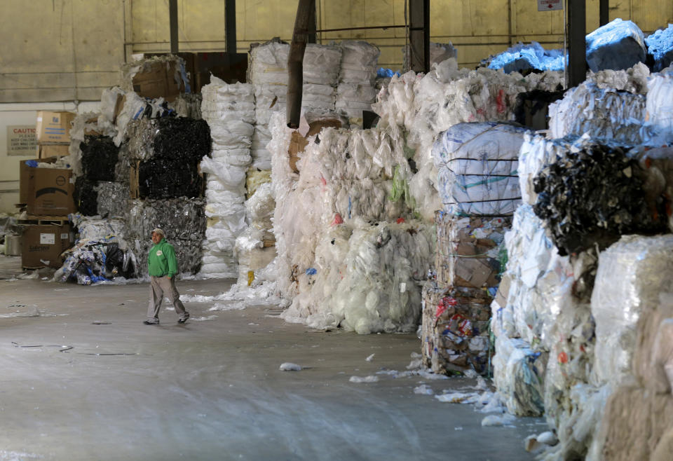 In this May 7, 2019 photo, a man walks under towers of recyclables at a GDB International warehouse in Monmouth Junction, N.J. A decision by China’s government to restrict imports of wastepaper and plastic that has disrupted U.S. recycling programs has also spurred investment in American plants that process recyclables. (AP Photo/Seth Wenig)