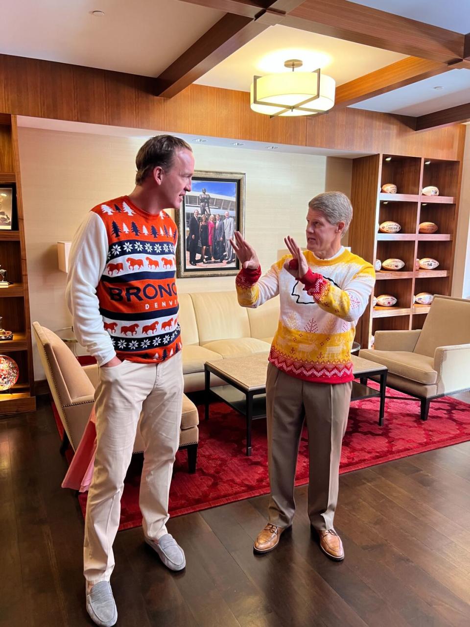 Clark Hunt talks to Peyton Manning, both in ugly Christmas sweaters, during a filming inside the in-stadium apartment.