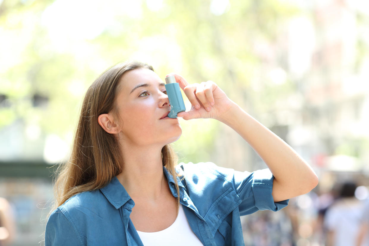 Asthmatic woman using inhaler standing in the street