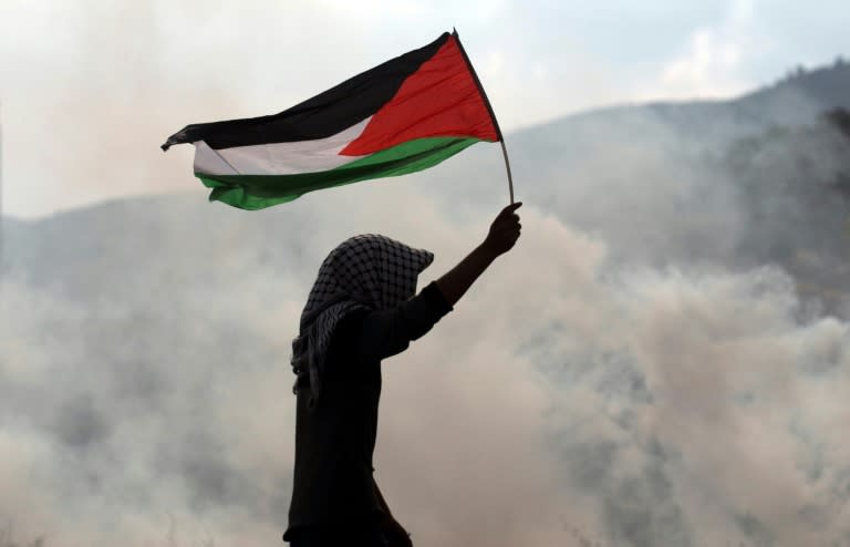 A protester waves a Palestinian flag amid tear gas during clashes with Israeli security forces near the Huwara checkpoint south of Nablus in the occupied West Bank on December 15, 2017