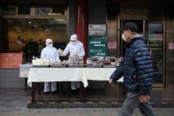 Restaurant workers wear protective clothing as they prepare food to sell on the street outside their restaurant in Beijing this week