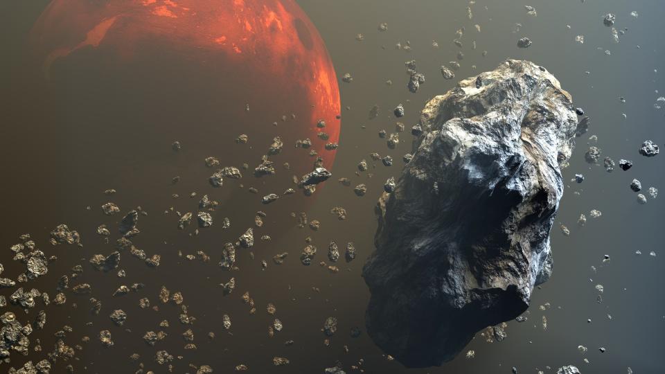     Rocky gray rocks float above a reddish orange planet. 