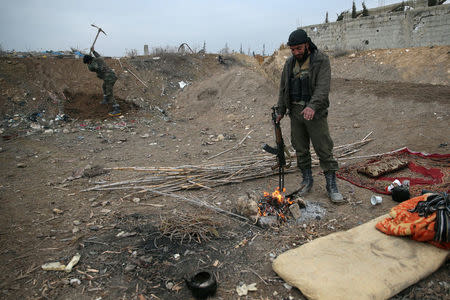 FILE PHOTO: A rebel fighter of Jaysh al-Islam warms himself near a fire, on al-Rayhan village front near the rebel held besieged Douma neighbourhood of Damascus, Syria January 2, 2017. REUTERS/Bassam Khabieh/File Photo