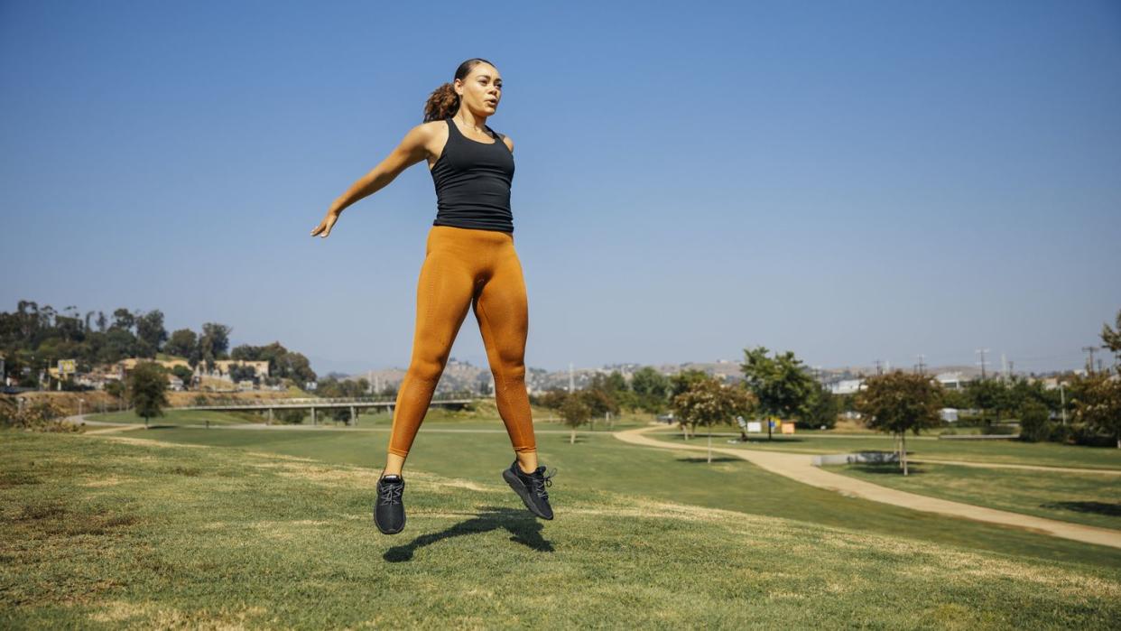 determined young women jumping while exercising at park against sky