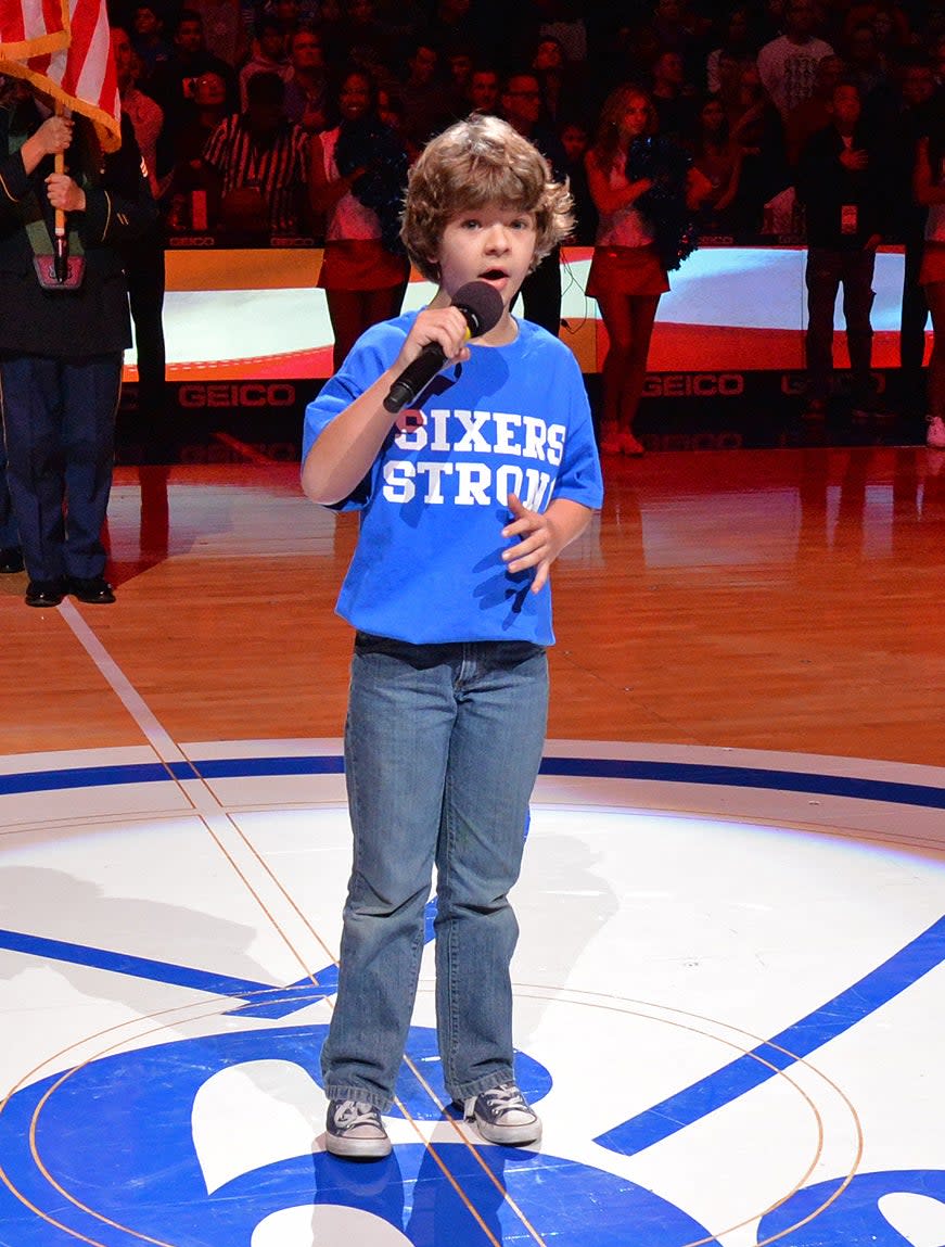 he's got long shaggy hair and wearing jeans and tee at a basketball game