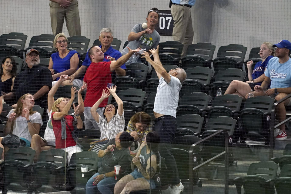 Fans reach up for a ball thrown to them by an Oakland Athletics player during a baseball game against the Texas Rangers, Wednesday, July 13, 2022, in Arlington, Texas. (AP Photo/Tony Gutierrez)