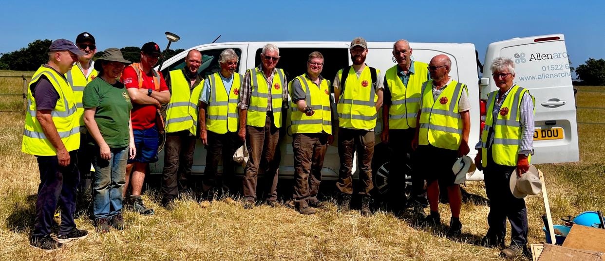 A group of people, many in bright yellow vests, standing in front of a white van, and the main in the center is holding a small metal dodecahedron