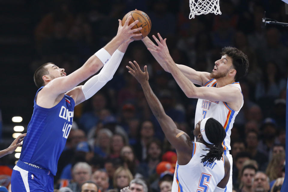 Los Angeles Clippers center Ivica Zubac (40) grabs a rebound next to Oklahoma City Thunder forward Chet Holmgren, upper right, and guard Luguentz Dort, lower right, during the first half of an NBA basketball game, Thursday, Feb. 22, 2024, in Oklahoma City. (AP Photo/Nate Billings)