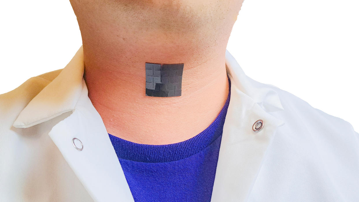  Photo shows a shiny black patch made up of small squares stuck to a man's throat; he's wearing a white button down over a blue t shirt. 