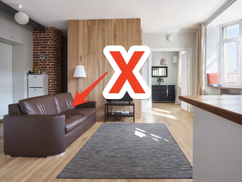 red x and arrow pointing at a faux brown leather couch in a living room with wooden details