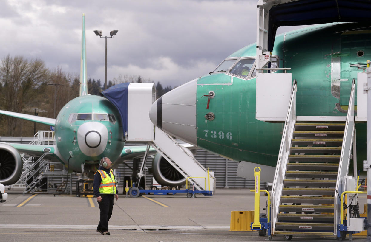 A worker looks up at a parked Boeing 737 Max 8 built for Jet Airways as another 737 Max 8 made for Shenzhen Airlines stands behind at a Boeing Co. production facility, Monday, April 8, 2019, in Renton, Wash. Boeing said the week before that it will cut production of its troubled 737 Max airliner in April, underscoring the growing financial risk it faces the longer that its best-selling plane remains grounded after two crashes. (AP Photo/Elaine Thompson)