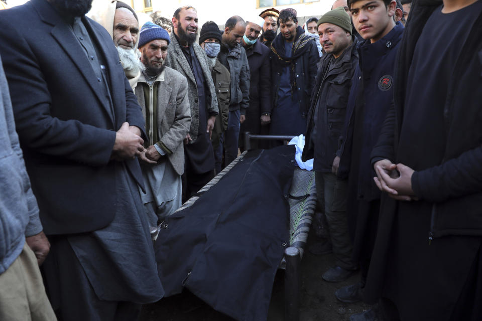 People gather around the body of man killed after a roadside bomb attack in Kabul, Afghanistan, Tuesday, Dec. 22, 2020. A roadside bomb tore through a vehicle in the Afghan capital of Kabul Tuesday, killing multiple people, police said. (AP Photo/Rahmat Gul)