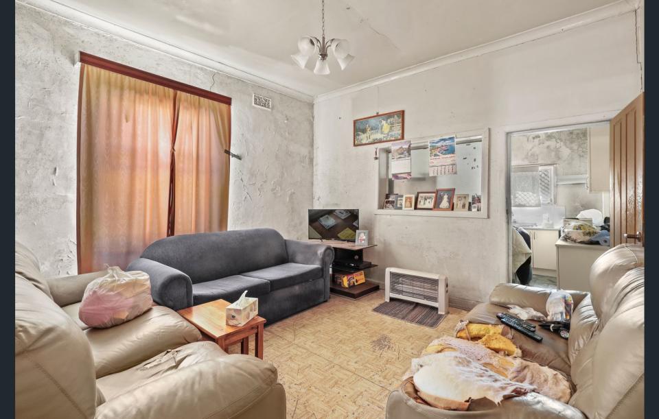 The living room of 25 Pine St, Newtown. The white paint on the walls is peeling off and three couches make up the room.