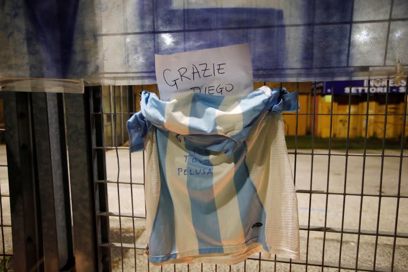 Una camiseta cuelga mientras la gente se reúne para llorar la muerte de la leyenda del fútbol argentino Diego Maradona afuera del estadio San Paolo en Nápoles, Italia.