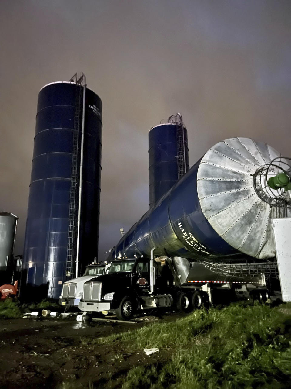 In this image provided by Karlie Eachus, a silo rests atop two tractor trailers at Wellacrest Farms moments in Mullica Hill, N.J. A tornado passes passed through the area on Wednesday, Sept. 1, 2021. (Karlie Eachus via AP)