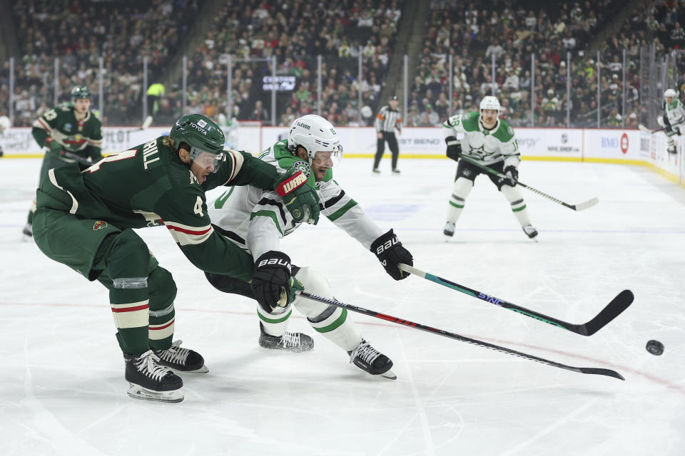 Minnesota Wild defenseman Jon Merrill, left, and Dallas Stars center Craig Smith (15) compete for the puck during the first period of an NHL hockey game Monday, Jan. 8, 2024, in St. Paul, Minn. (AP Photo/Matt Krohn)