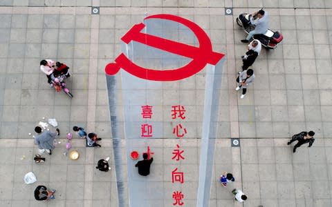 A man in central China works on a 3D street painting of the emblem of Chinese Communist Party to celebrate the upcoming party congress  - Credit: AFP