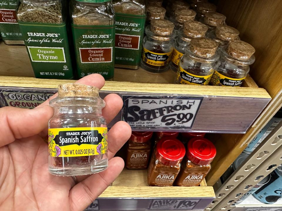 hand holding small jar of spanish saffron in front of the spice shelves at trader joes