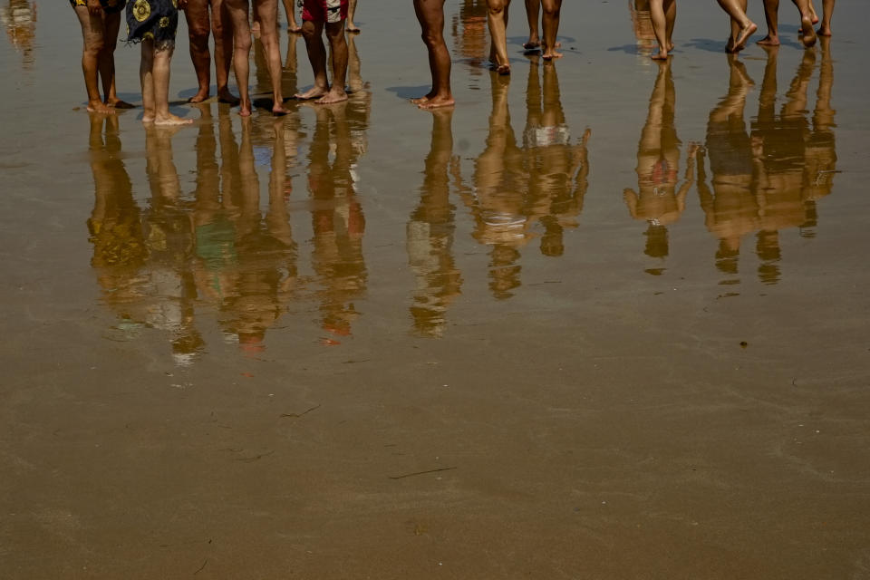 People reflected on the sand while walking along the beach in Laredo, northern, Spain Monday, July 18, 2022. (AP Photo/Alvaro Barrientos)