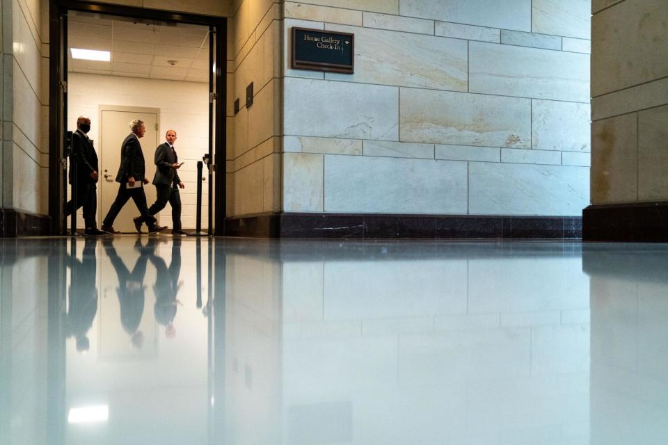 Three men walk down a hall in a building.