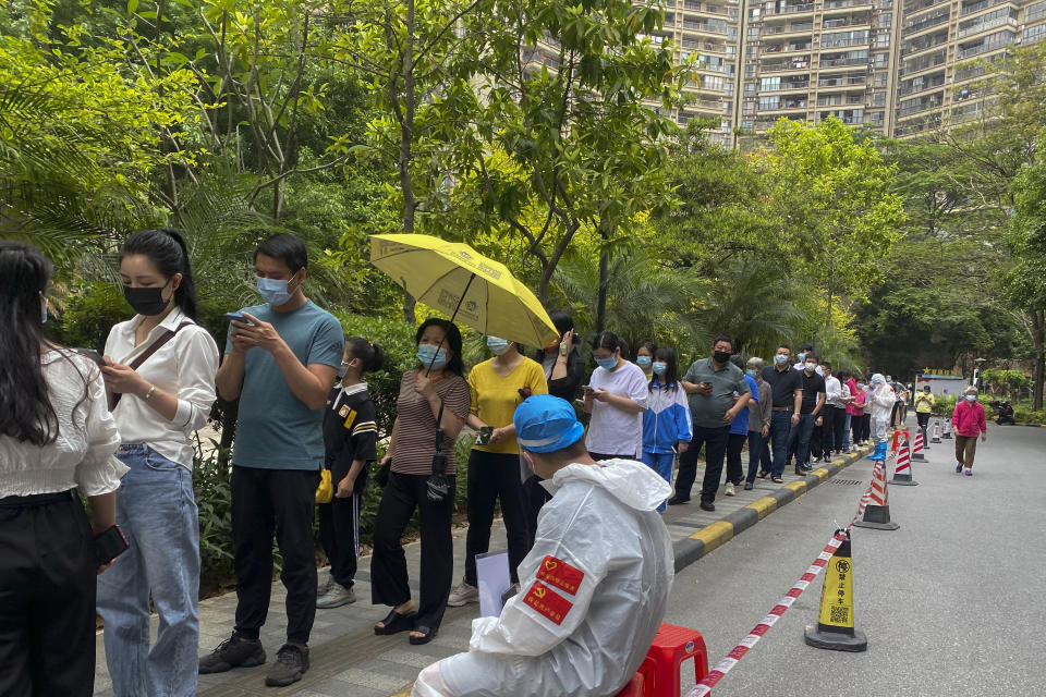 Workers in protective gear watch over residents line up for the COVID-19 test at a residential block, Monday, April 11, 2022, in Guangzhou in south China's Guangdong province. The manufacturing hub of Guangzhou began tightly restricting departures and arrivals Monday as eastern China battles the country's latest major COVID outbreak. (Chinatopix Via AP)